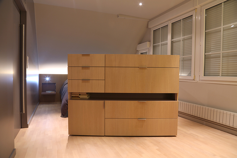 Agencement intérieur sur mesure par LDC Agencement – L’Arche du Bois : tiroirs en bois au centre de la chambre avec fenêtres à droite, mobilier moderne et rangement personnalisé.