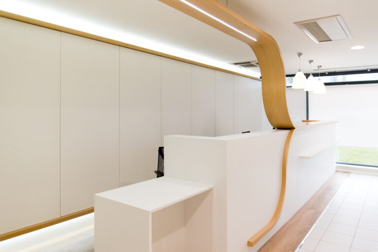 Comptoir d’accueil blanc orné d’éléments décoratifs en bois, avec un éclairage LED intégré apportant une touche moderne — une réalisation sur mesure signée Arche du Bois, alliant clarté et raffinement.