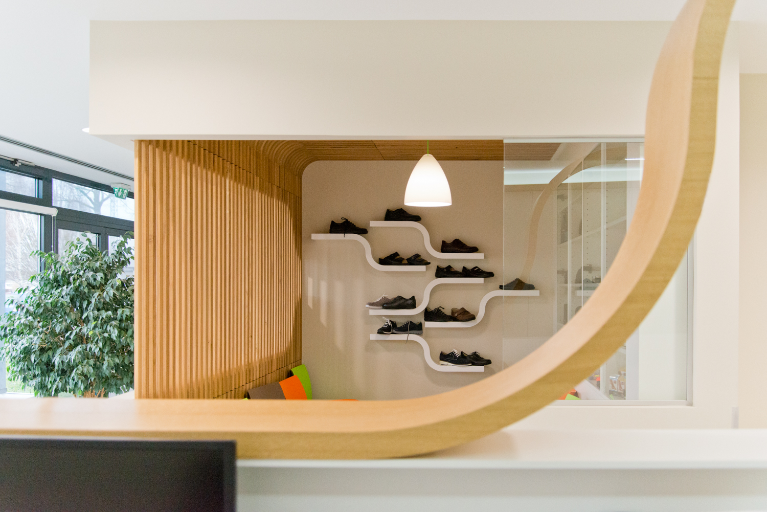 Mur en lames de bois verticales sur la gauche, face à une série d’étagères garnies de chaussures, avec des assises installées en bas à gauche — un agencement pratique et chaleureux conçu par Arche du Bois.