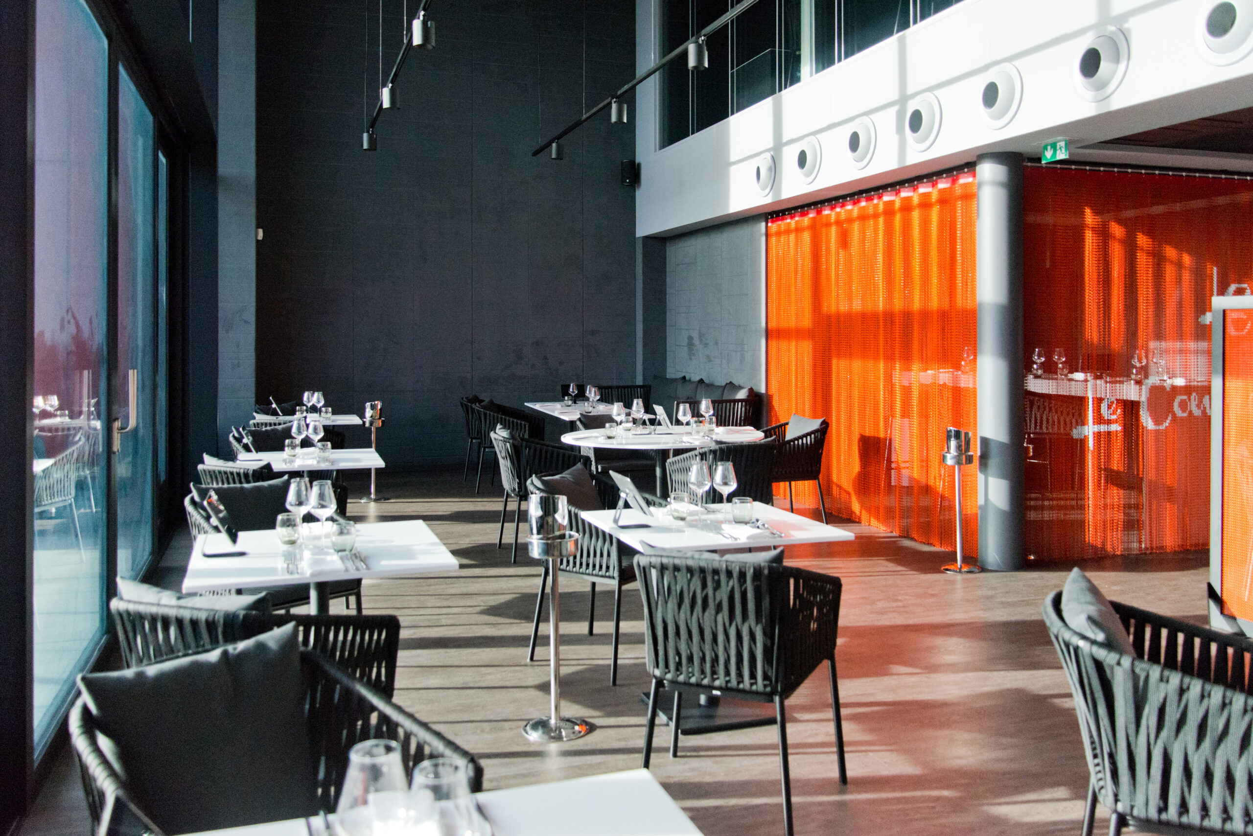 Salle à manger spacieuse avec plafond haut, aménagée avec plusieurs tables et chaises en bois — un agencement raffiné et aéré signé Arche du Bois, offrant une ambiance chic et chaleureuse grâce à la qualité des matériaux et à l’élégance des volumes.