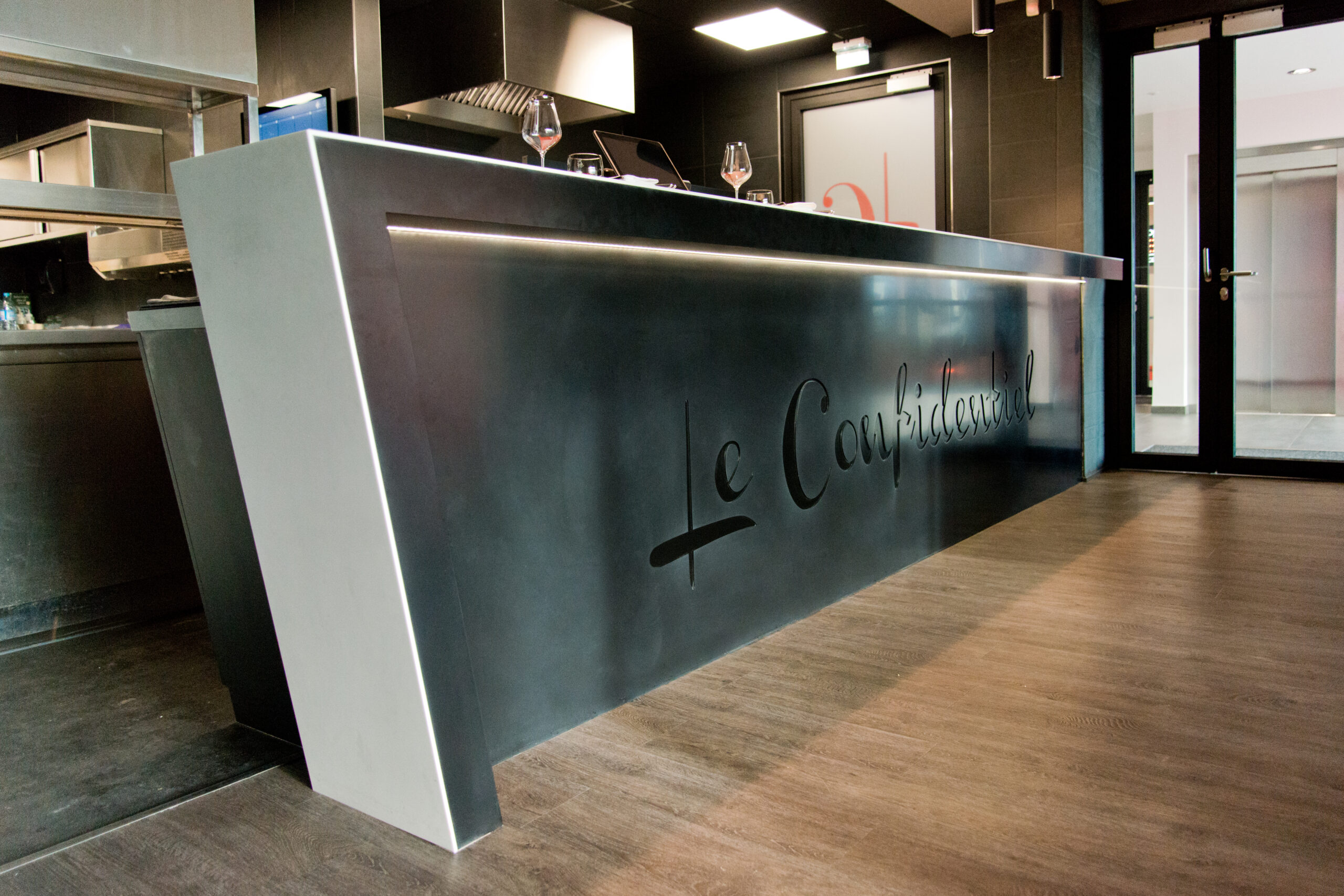 Comptoir de bar noir avec éclairage LED intégré en partie basse, et une porte visible sur le côté droit de l’image