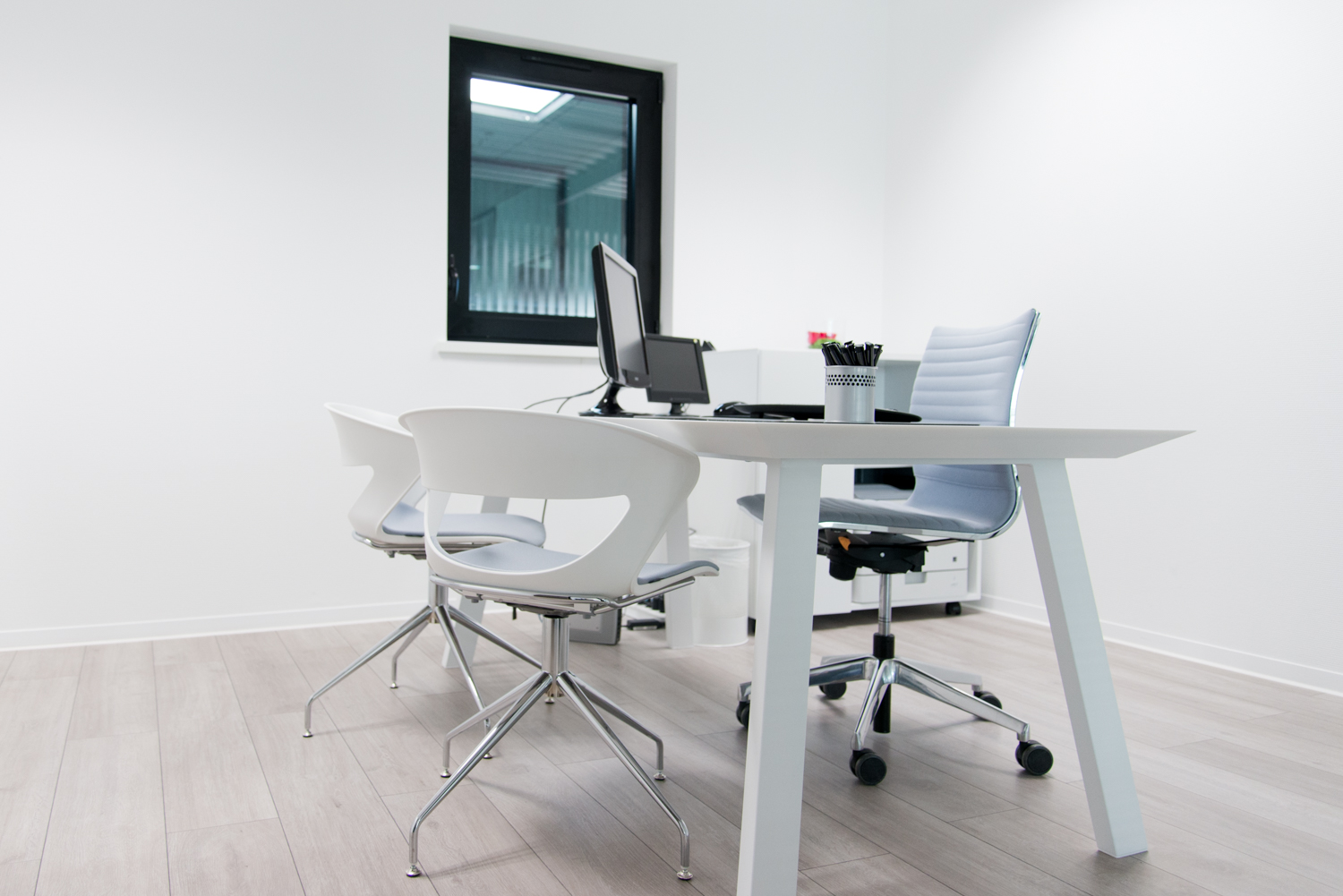 Table accompagnée de trois chaises placée au centre de la pièce, avec une fenêtre sur le mur en face — un agencement épuré et lumineux réalisé par Arche du Bois pour un espace fonctionnel et convivial.
