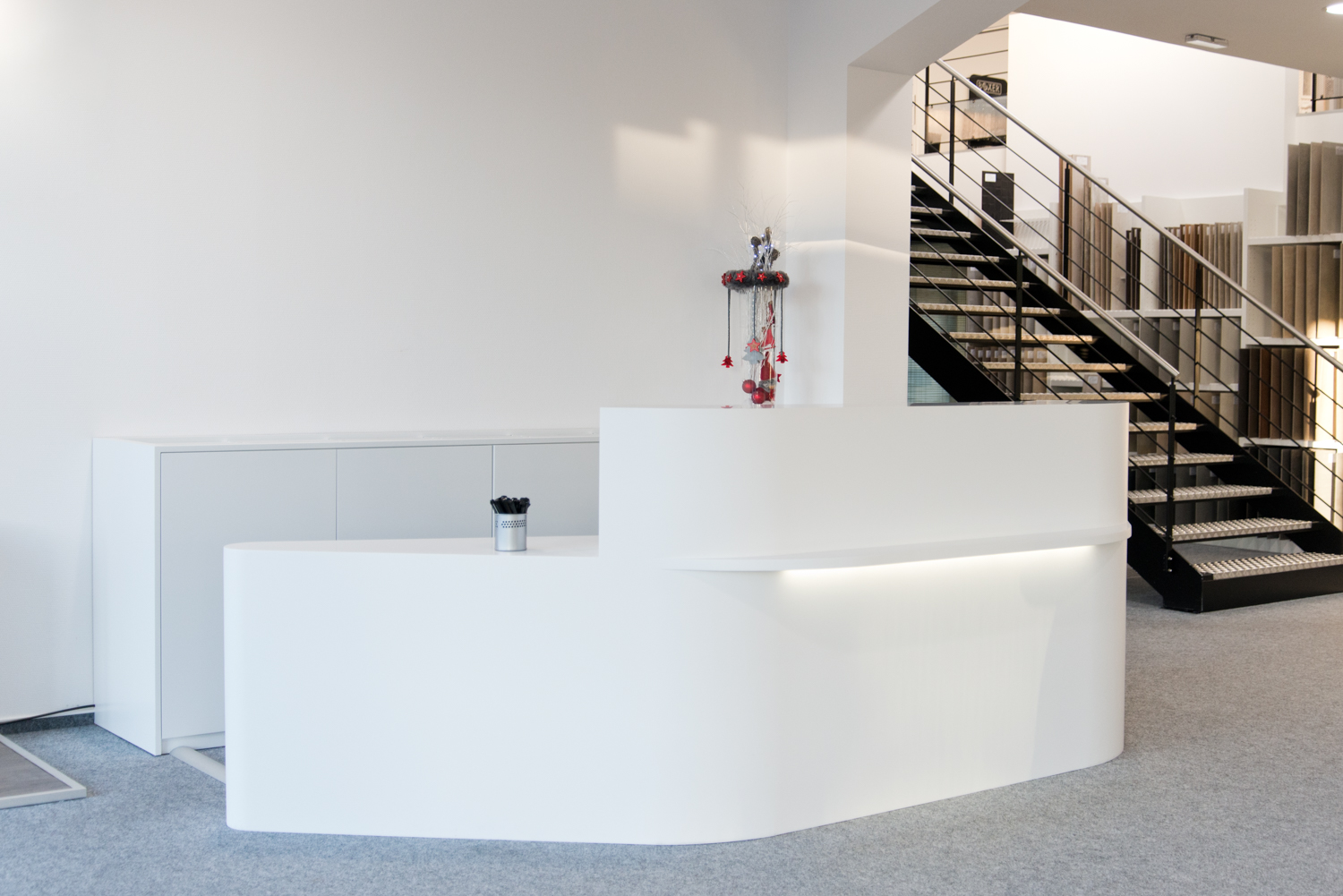 Comptoir blanc au design épuré, situé à côté d’un escalier intérieur — un agencement harmonieux et fonctionnel réalisé par Arche du Bois, intégrant circulation verticale et espace d’accueil.