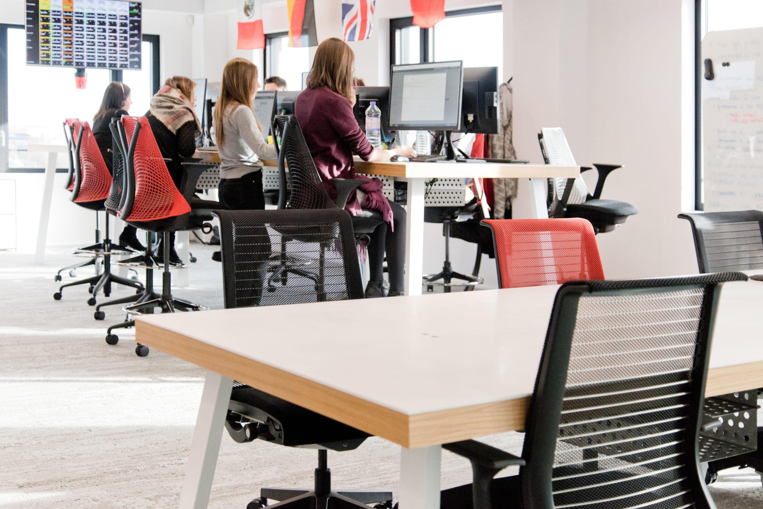 Vue rapprochée d’une table en bois avec, à l’arrière-plan, plusieurs bureaux et chaises occupés par des personnes travaillant sur ordinateur