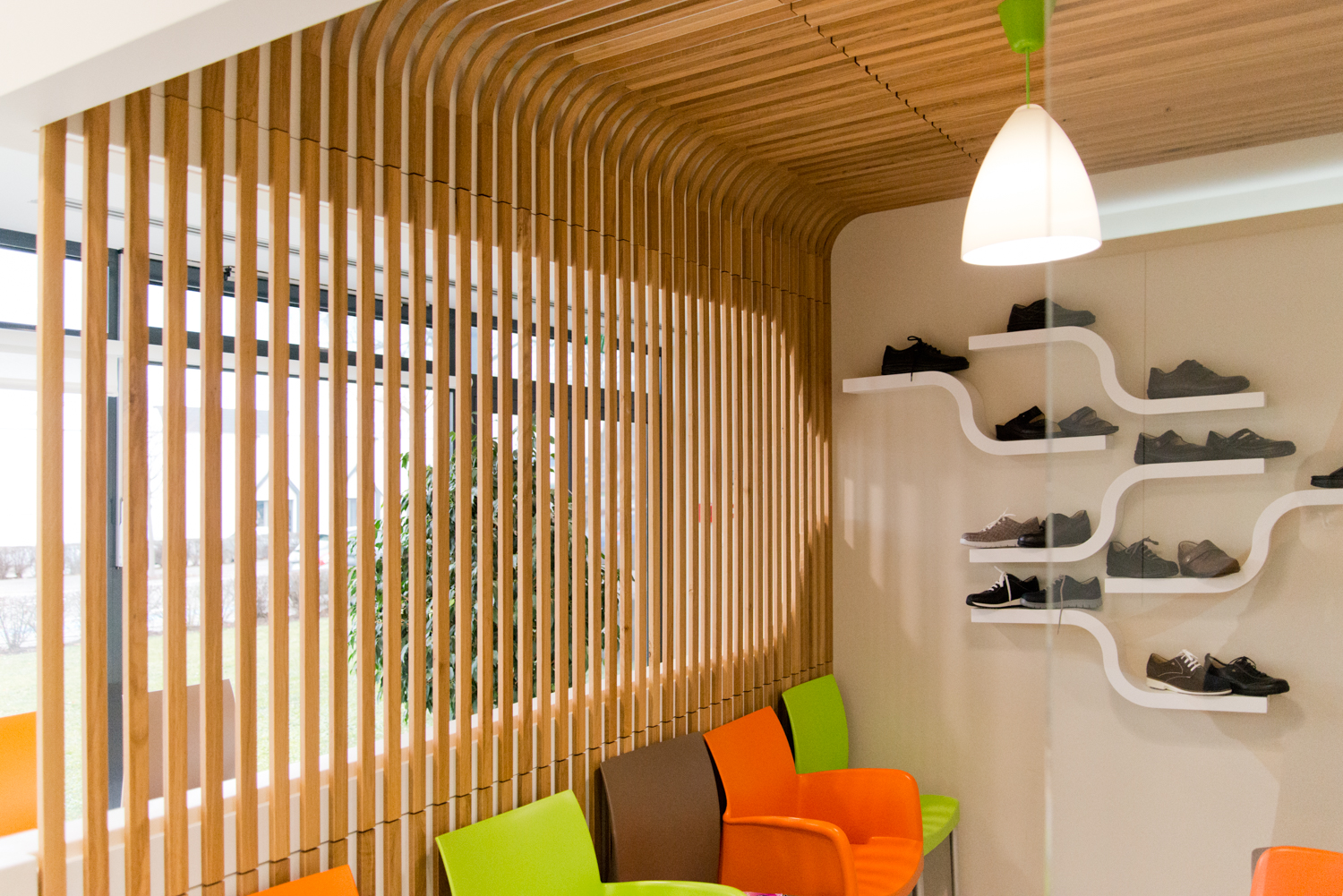 Mur en lames de bois verticales sur la gauche, face à une série d’étagères garnies de chaussures, avec des assises installées en bas à gauche — un agencement pratique et chaleureux conçu par Arche du Bois.