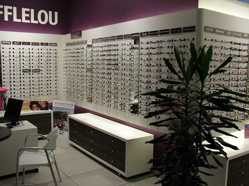 Étagères murales alignées exposant une large sélection de lunettes, organisées de manière claire et ordonnée — un agencement soigné conçu pour une présentation optimale en magasin d’optique.