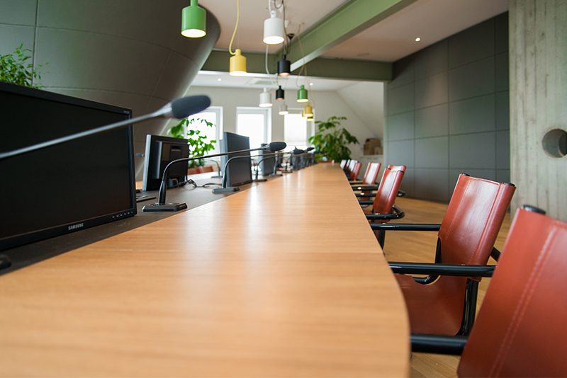 Table de conférence entourée de plusieurs chaises, avec un microphone et un écran individuel devant chaque siège