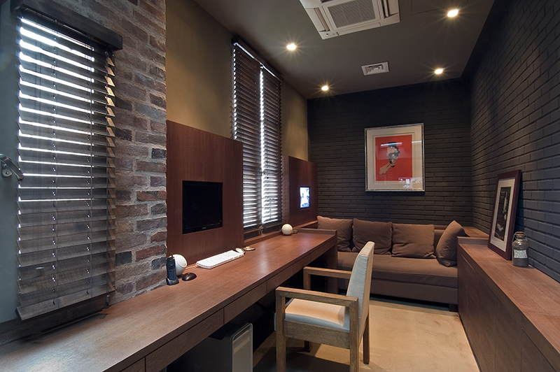 Petit bureau avec un canapé au fond de la pièce, des fenêtres sur la gauche laissant entrer la lumière naturelle, un grand plan de travail sur toute la longueur et une armoire de rangement sur la droite — un aménagement compact et fonctionnel réalisé par Arche du Bois.