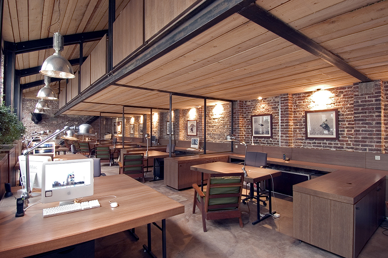 Espace de travail avec murs en briques apparentes, plafond en bois et postes informatiques installés sur chaque bureau — un environnement professionnel au style industriel et naturel, conçu par Arche du Bois pour allier fonctionnalité et esthétique authentique.