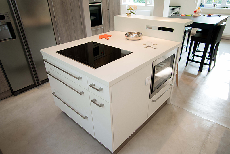 Îlot central blanc équipé de tiroirs et placards intégrés, surmonté d’une plaque de cuisson vitrocéramique noire. Un four encastré complète cet espace fonctionnel au design épuré, idéal pour une cuisine contemporaine