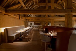 Salle à manger avec, à droite, des tables individuelles accompagnées de chaises, et à gauche, des tables carrées alignées formant un espace collectif avec une banquette continue