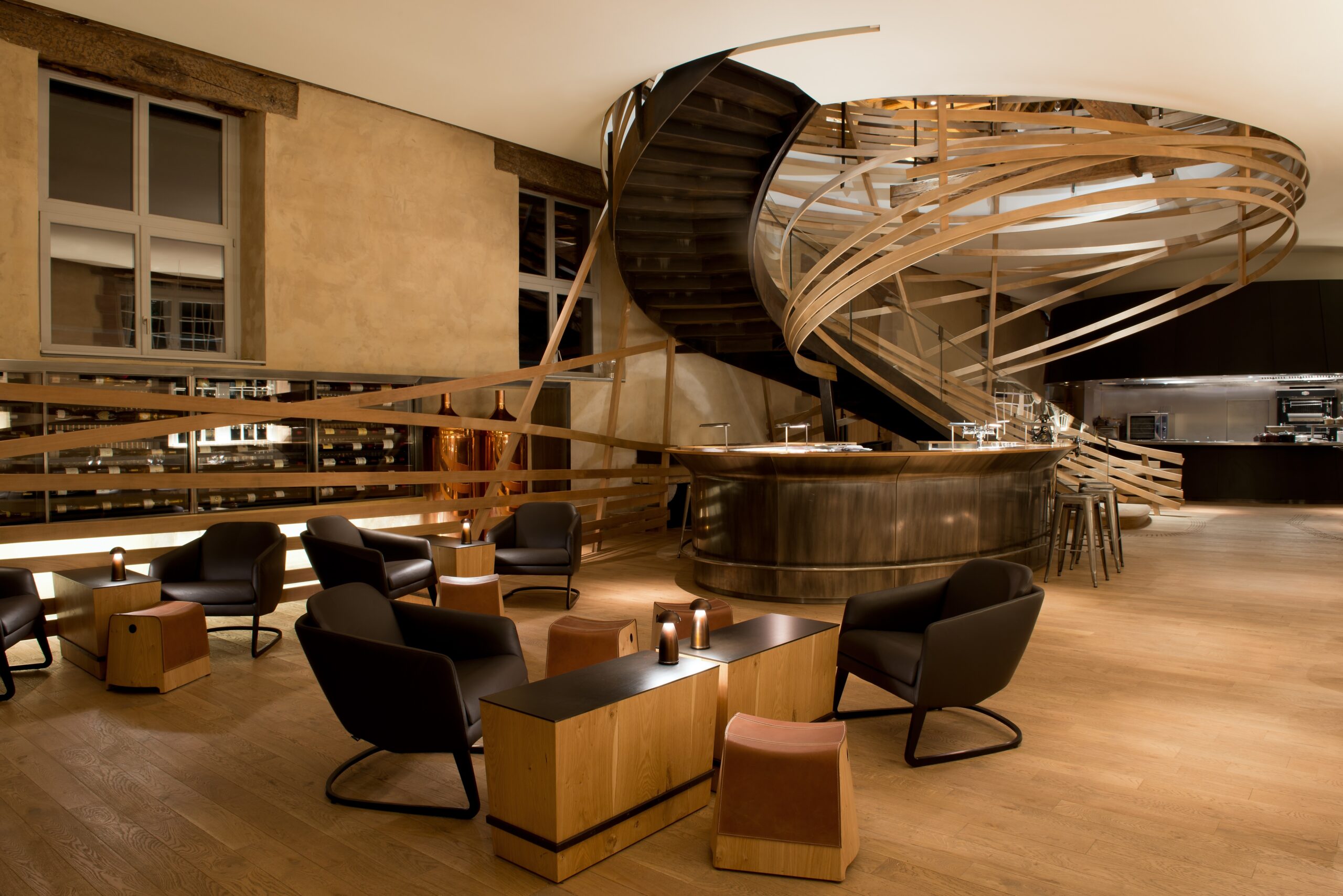 Plusieurs tables et chaises disposées dans la pièce, avec un escalier en bois courbe menant à l’étage supérieur