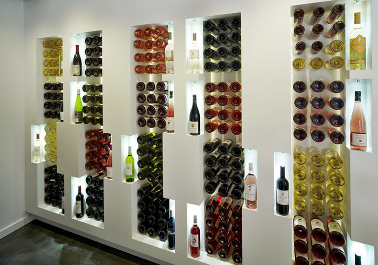 Bouteilles de vin soigneusement alignées sur des étagères en bois, dans une disposition ordonnée et esthétique — un agencement sur mesure réalisé par Arche du Bois pour la mise en valeur de produits d’exception.