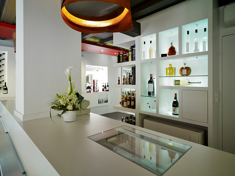 Table décorative avec un vase au centre, placée devant des étagères en bois remplies de bouteilles d’alcool — un agencement raffiné signé Arche du Bois, mêlant décoration naturelle et présentation élégante des spiritueux.