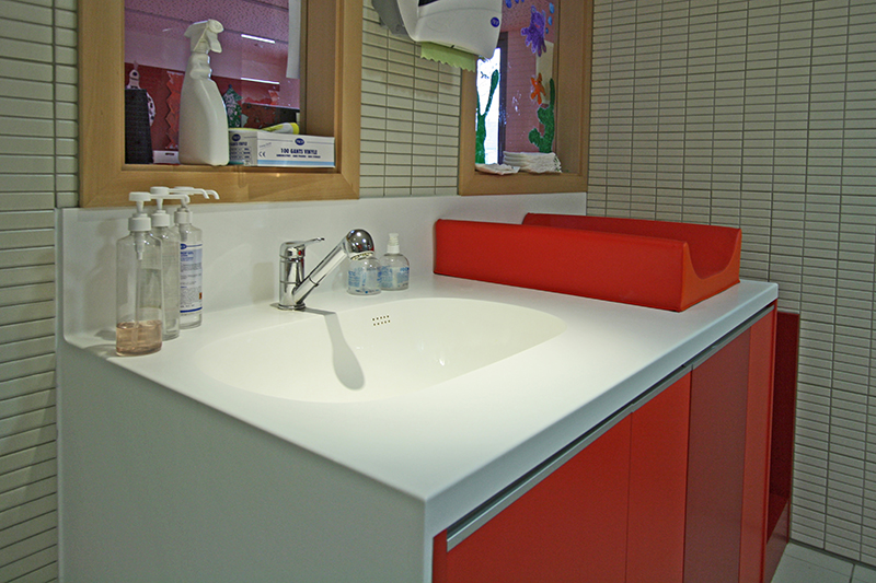 Meuble vasque rouge avec plan vasque blanc, installé face à un mur équipé de deux miroirs muraux — un agencement élégant et fonctionnel signé Arche du Bois.