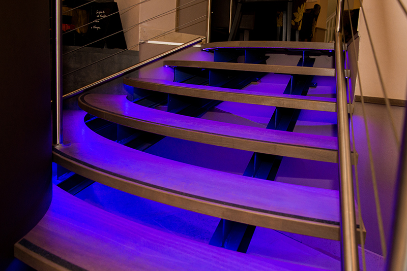 Éclairage LED intégré sous un escalier, créant un jeu de lumière subtil et moderne