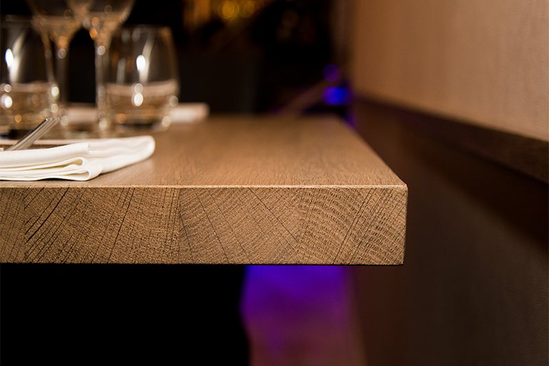 Détail du coin d’une table en bois, mettant en avant la finition soignée et la texture naturelle du matériau