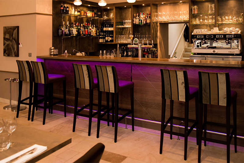Bar en bois avec plusieurs tabourets alignés à l’arrière, et un éclairage LED intégré sous le comptoir