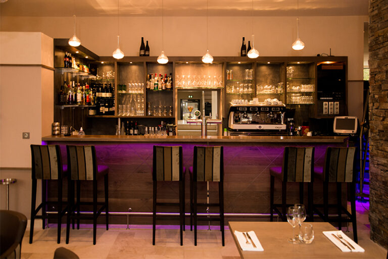 Bar en bois avec plusieurs tabourets alignés à l’arrière, et un éclairage LED intégré sous le comptoi