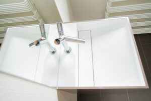 Vue de dessus d’une vasque blanche avec robinet en acier et miroir latéral, intégrée dans un projet d’agencement de salle de bain sur mesure réalisé par L’Arche du Bois, entreprise de menuiserie et d’aménagement intérieur en Alsace et en France.