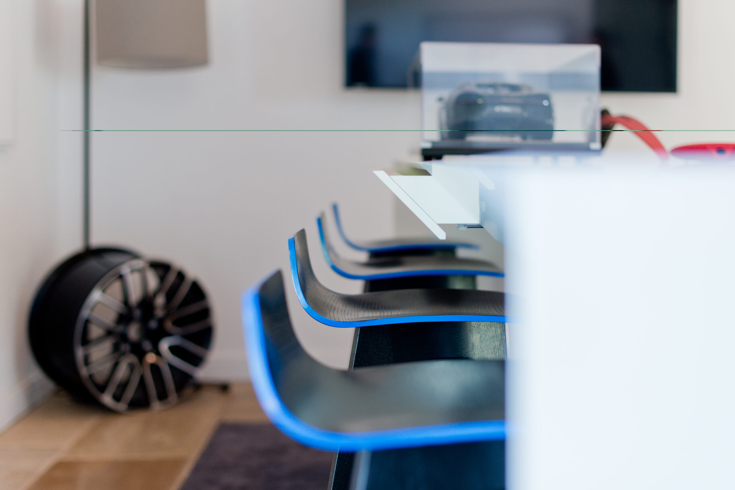 Plusieurs chaises disposées derrière une table blanche, sur laquelle repose une maquette de voiture Bugatti ; à l’arrière gauche de l’image, un jante de voiture sportive est également visible
