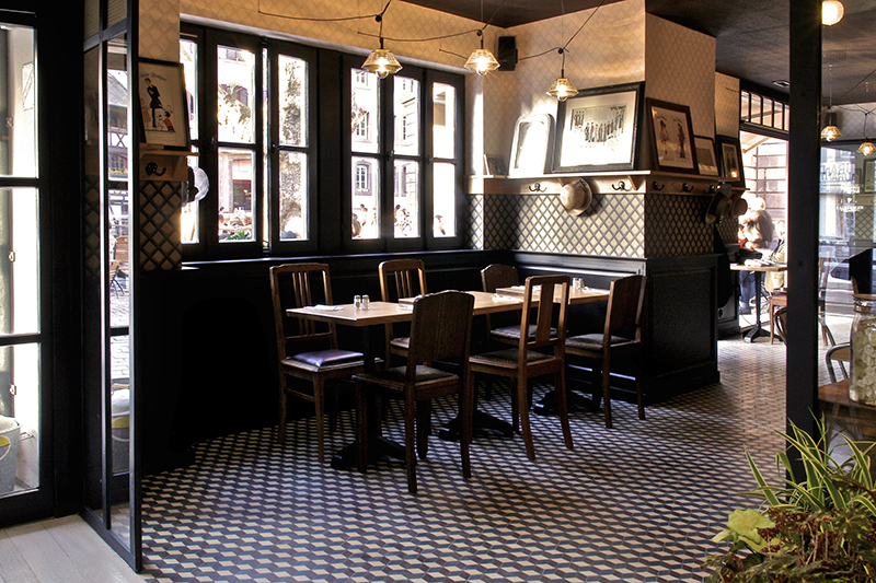 Deux ensembles table et chaises placés face à une fenêtre, dans un espace à l’atmosphère traditionnelle — un agencement authentique signé Arche du Bois, combinant mobilier en bois et charme intemporel.