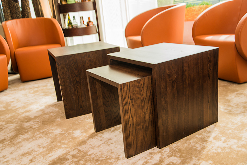 Deux tables en bois placées au centre de l’image, entourées de plusieurs fauteuils en cuir confortables — un agencement élégant et accueillant signé Arche du Bois, alliant matériaux nobles et confort d’assise.