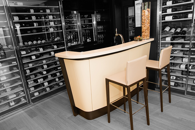 Espace accueil avec deux chaises placées en face, entouré de vitrines à portes vitrées en arrière-plan et sur le côté, exposant des bouteilles de vin — un agencement raffiné et fonctionnel signé Arche du Bois, mêlant confort d’accueil et présentation soignée.