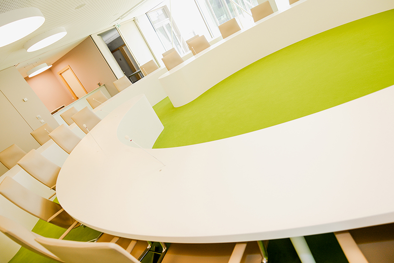 Table de conférence ronde blanche entourée de chaises assorties, installée sur un sol vert vibrant