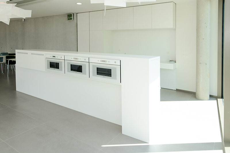 Plan de travail blanc avec trois micro-ondes intégrés, installé devant un ensemble d’armoires blanches