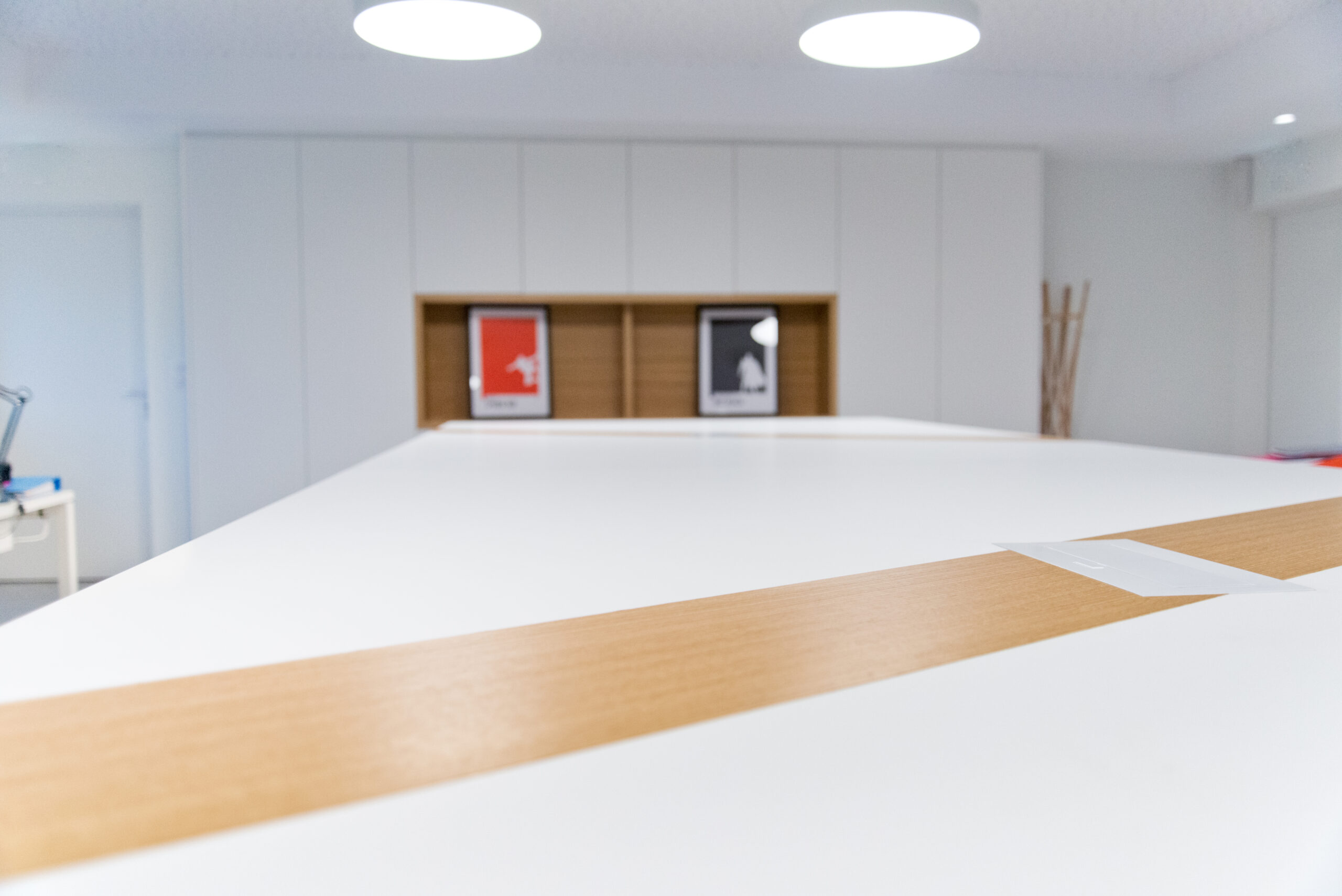 Vue depuis une table, avec à l’arrière-plan plusieurs armoires de rangement et deux suspensions lumineuses positionnées au-dessus du meuble