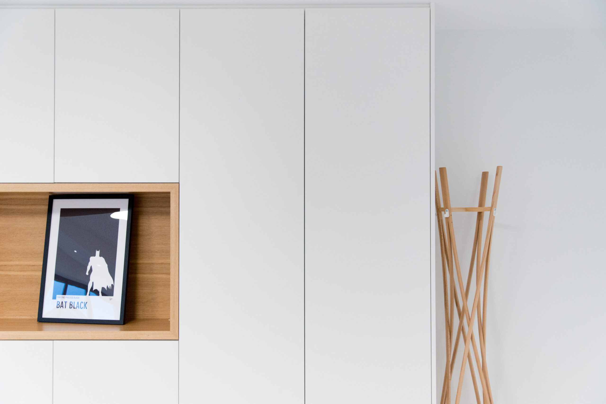 Armoire blanche intégrant une niche centrale de type étagère, dans laquelle est posé un cadre photo décoratif ; un présentoir en bois se trouve à côté du meuble