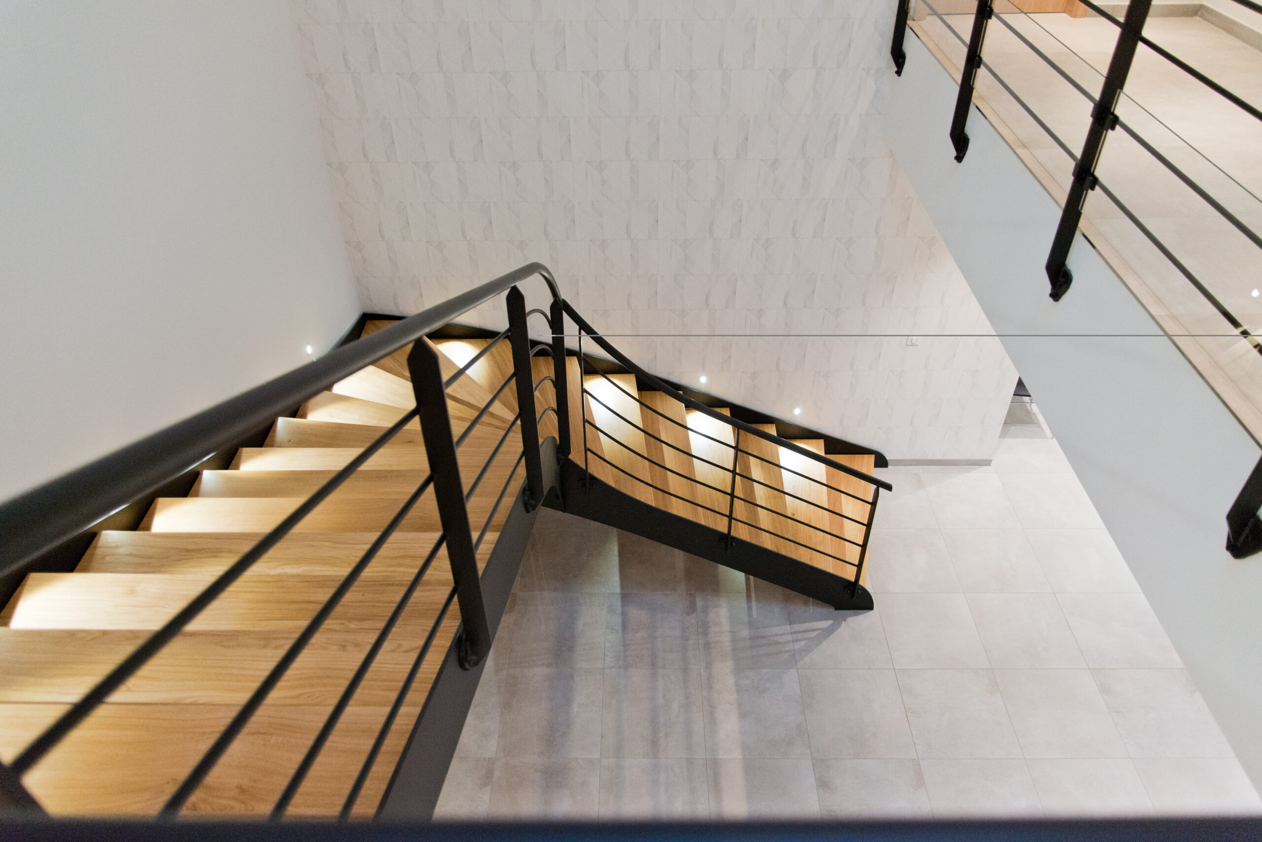 Escalier en bois avec garde-corps métalliques noirs, encadré par des murs blancs