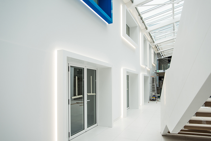 Vue intérieure montrant à gauche un mur avec plusieurs portes et fenêtres encadrées par un éclairage LED, et à droite l’arrière d’un escalier design — une réalisation soignée d’Arche du Bois alliant lumière et architecture boisée