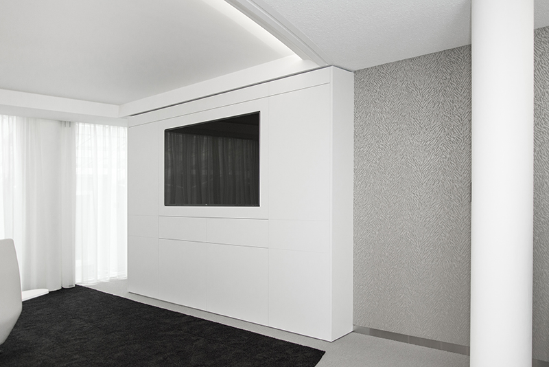 Mur blanc avec un écran intégré en son centre, accompagné d’un rideau installé sur la gauche