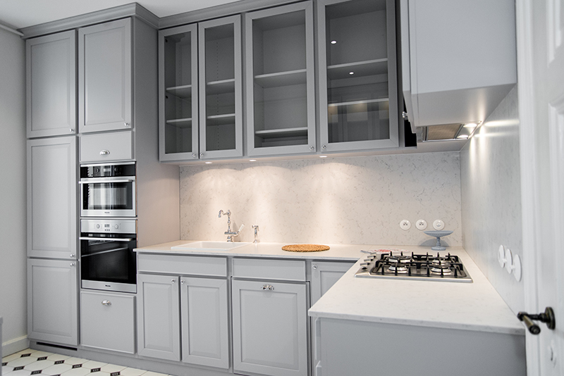 Cuisine équipée signée Arche du Bois avec un agencement fonctionnel : plaque de cuisson encastrée sur le plan de travail à droite, rangements hauts et bas en face, four et micro-ondes intégrés dans les colonnes à droite