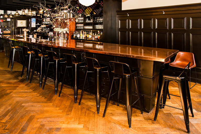 Long comptoir de bar entouré de plusieurs tabourets, conçu par Arche du Bois pour offrir un espace convivial et élégant adapté aux moments de partage et de détente.