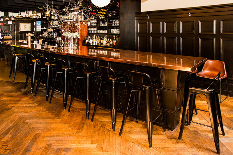 Long comptoir de bar entouré de plusieurs tabourets, conçu par Arche du Bois pour offrir un espace convivial et élégant adapté aux moments de partage et de détente.