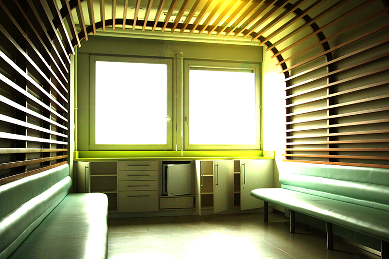 Espace intérieur avec plafond voûté, deux fenêtres en fond de pièce, et deux banquettes intégrées courant le long des murs latéraux — un agencement élégant et structuré réalisé par Arche du Bois.