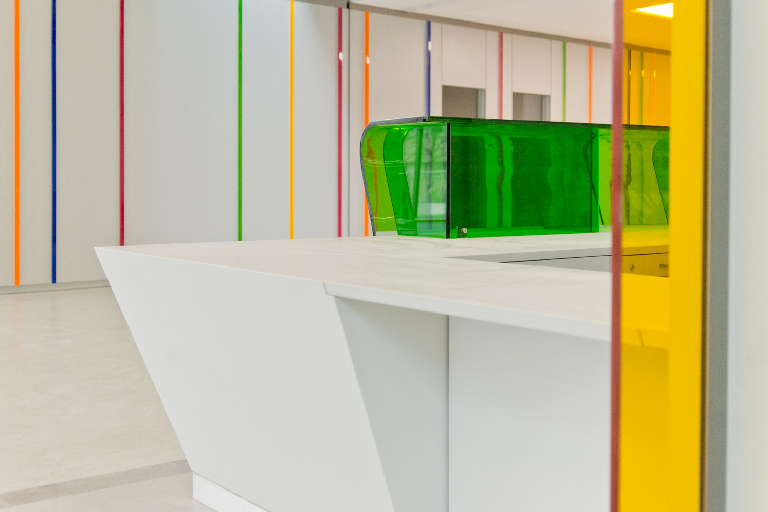 Espace accueil blanc conçu par Arche du Bois, sublimé par des éléments décoratifs en verre coloré, apportant luminosité et raffinement à l’aménagement.