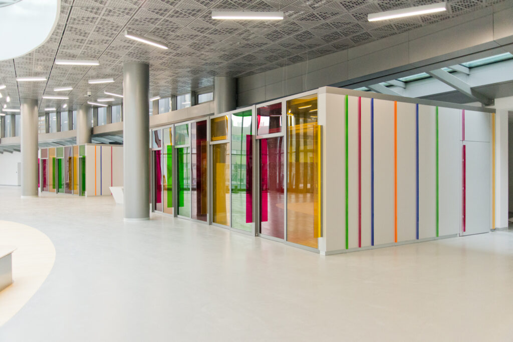 Deux pièces aux murs blancs décorés de lignes colorées, avec des portes vitrées teintées — un agencement contemporain et dynamique conçu par Arche du Bois, mêlant clarté et identité visuelle forte.