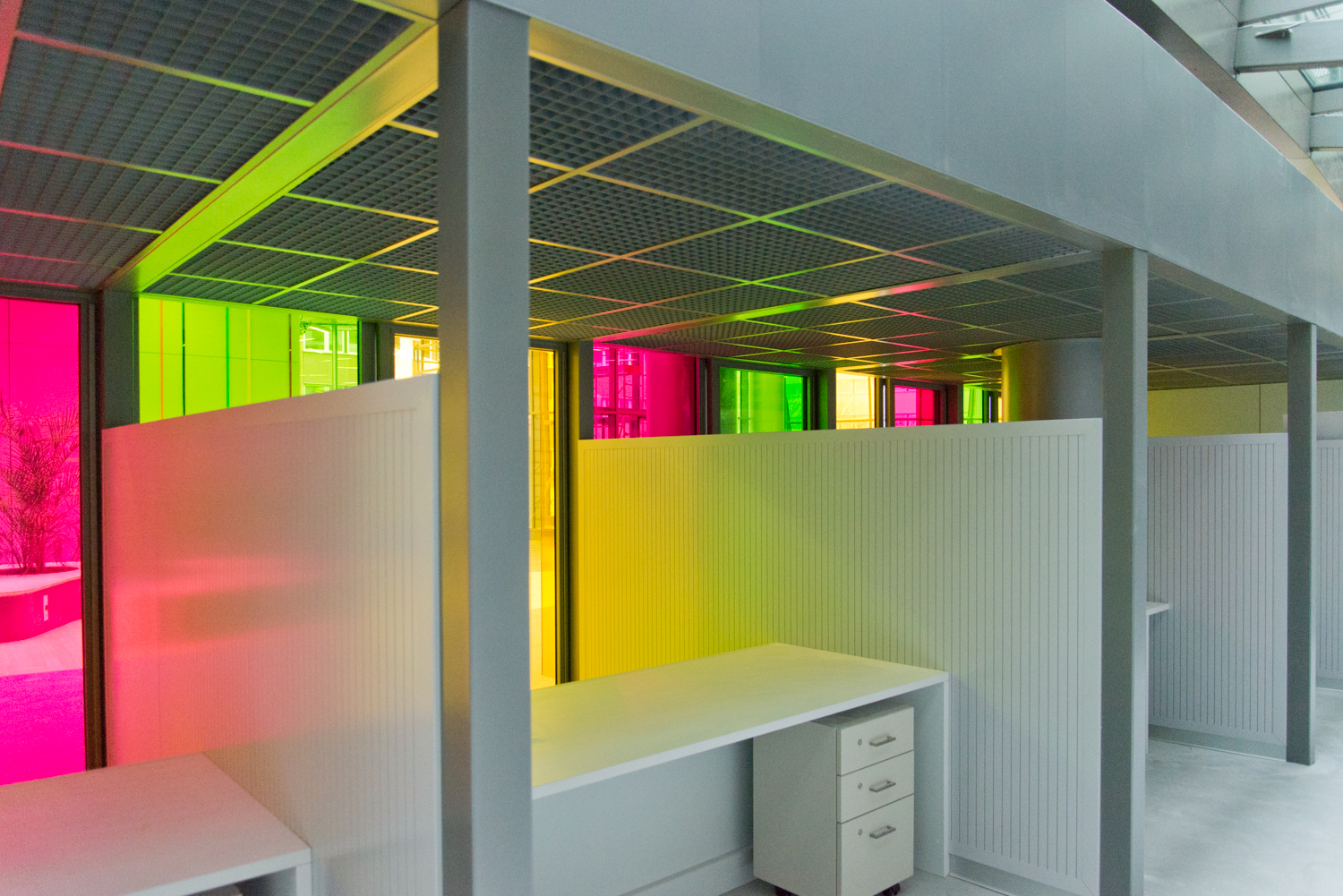 Espaces de travail séparés par des cloisons, chacun équipé d’un bureau individuel, avec en façade des vitres colorées laissant passer la lumière — un agencement fonctionnel et esthétique conçu par Arche du Bois.
