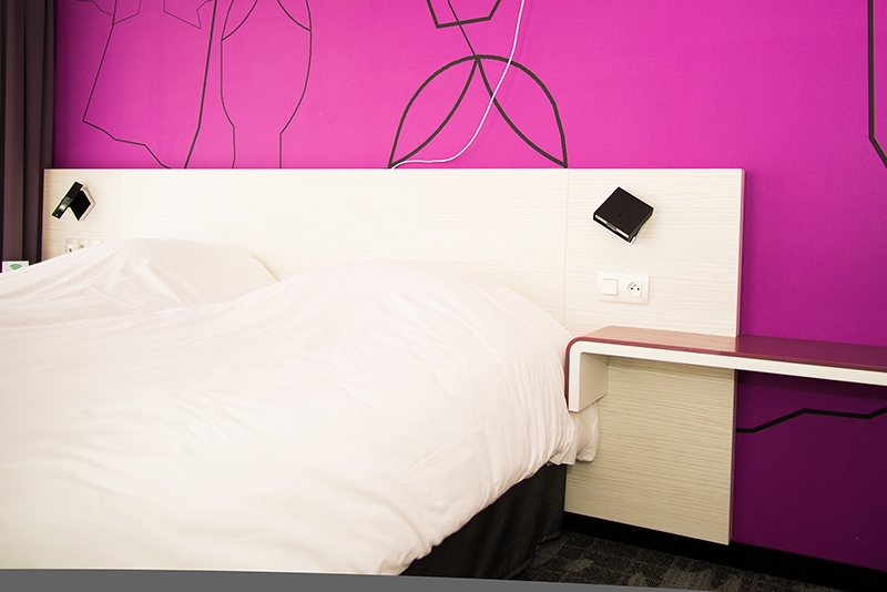 Lit double placé devant un mur d’accent violet, créant une atmosphère élégante et apaisante