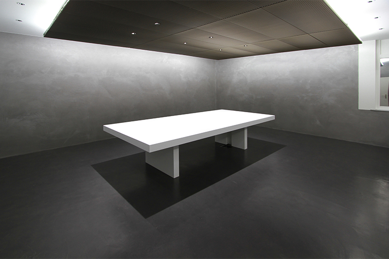 Grande table blanche installée dans une pièce aux murs noirs, sublimée par un éclairage suspendu