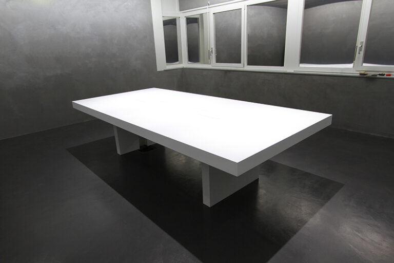 Grande table blanche installée dans une pièce aux murs noirs, sublimée par un éclairage suspendu