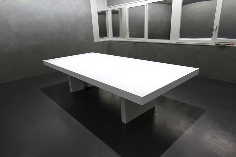 Grande table blanche installée dans une pièce aux murs noirs, sublimée par un éclairage suspendu