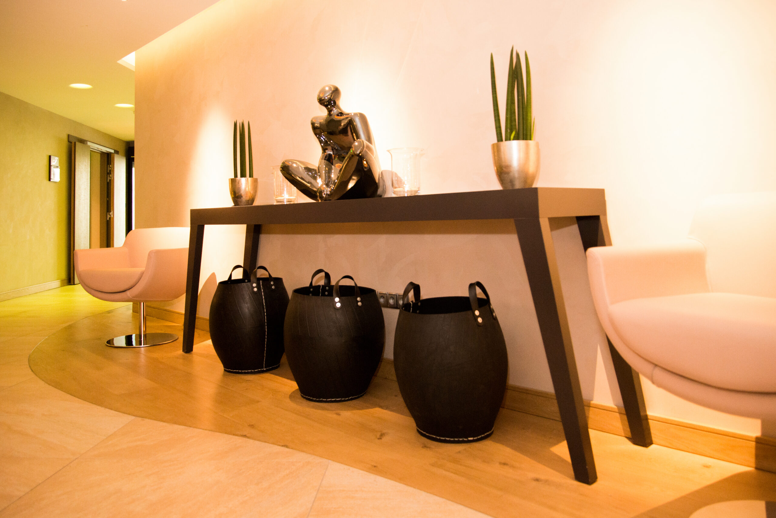 Table en bois aux pieds inclinés, décorée d’une sculpture centrale encadrée par deux vases, avec deux fauteuils de part et d’autre, et trois jarres noires placées en dessous