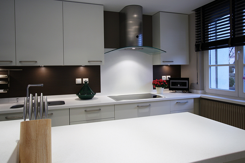 Cuisine sur mesure par LDC Agencement – L’Arche du Bois : placards hauts au fond, tiroirs en bas, plaque de cuisson avec hotte, et fenêtre à droite.