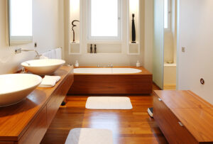Salle de bain sur mesure avec baignoire en fond, double vasque avec robinetterie à gauche et meuble de rangement à droite, sol et mobilier en bois, agencement intérieur réalisé par L’Arche du Bois, entreprise de menuiserie en Alsace intervenant en France.
