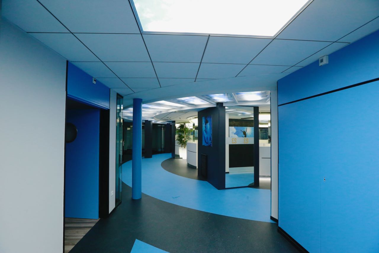 Couloir menant à un espace accueil circulaire à l’ambiance bleue, conçu par Arche du Bois — une transition fluide entre circulation et zone d’accueil au design immersif.